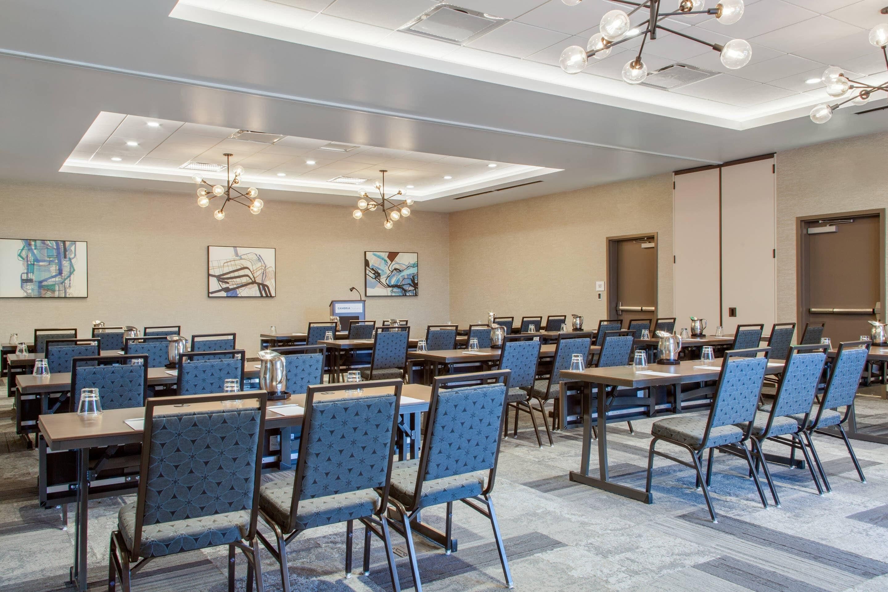 A conference room with multiple tables and chairs, ceiling lights, and artwork on the walls.