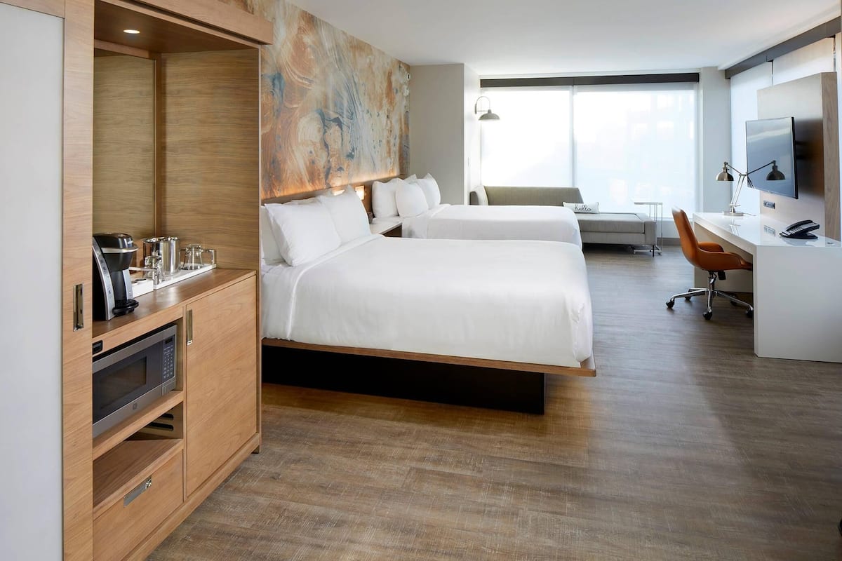 Une chambre d’hôtel avec deux lits, un bureau, une télévision, une machine à café et un grand tableau abstrait accroché au mur.