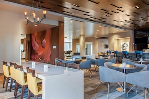 A modern hotel lobby with a marble reception desk, multiple seating areas, and a large abstract wall art piece.