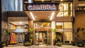 A hotel entrance with a revolving door, a sign for 'CAMBRIA HOTEL', and a 'Cafeteria' sign.