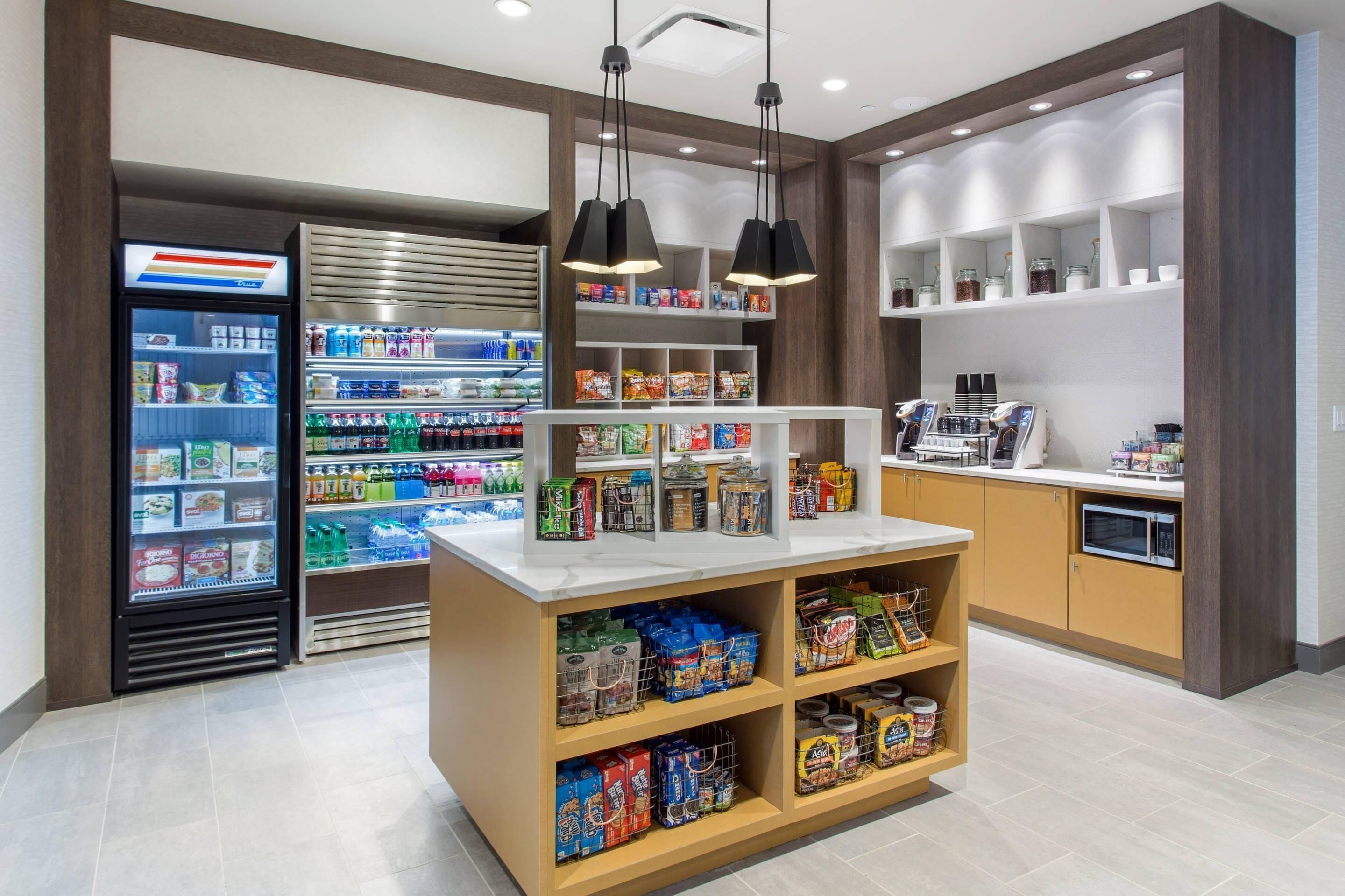 A well-lit convenience store with refrigerated and non-refrigerated sections, shelves stocked with snacks, and a coffee machine.