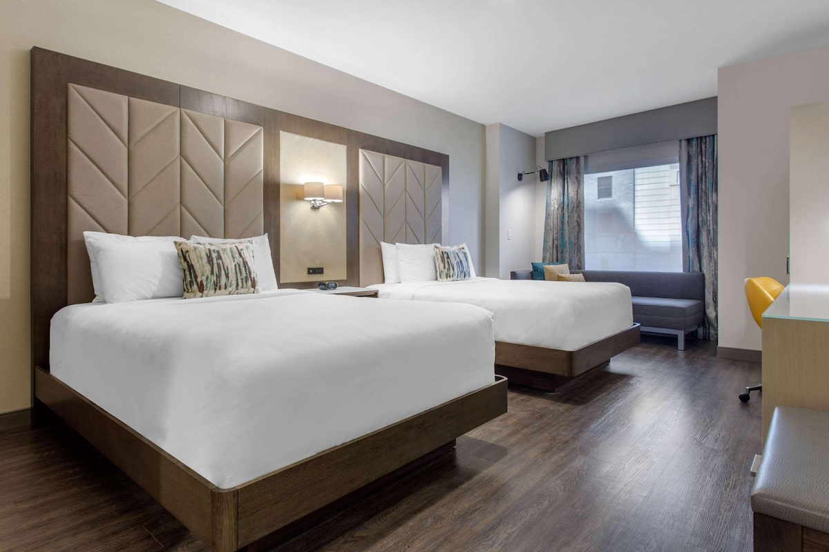 Ein Hotelzimmer mit zwei Betten, einem Schreibtisch und einem Fenster mit Vorhängen.