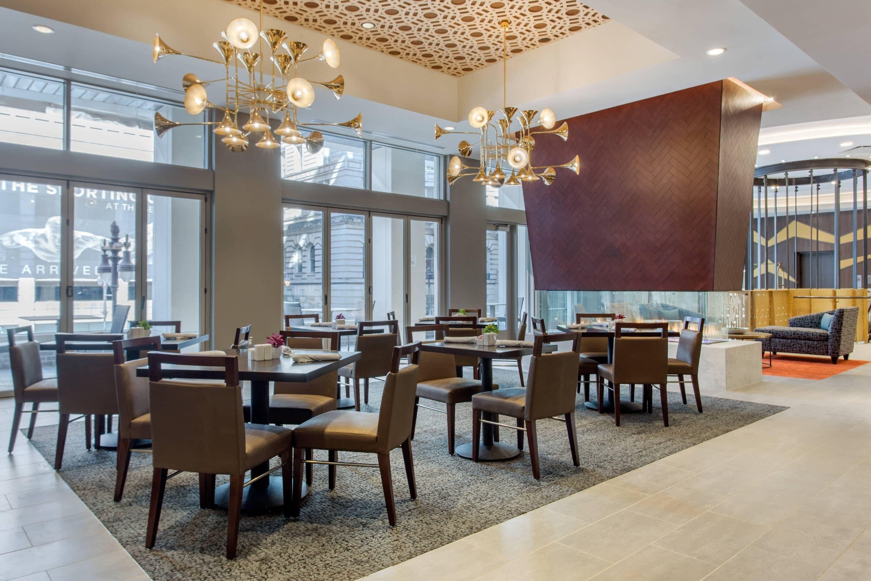 A modern dining area with multiple tables and chairs, large windows, and a decorative ceiling light fixture.