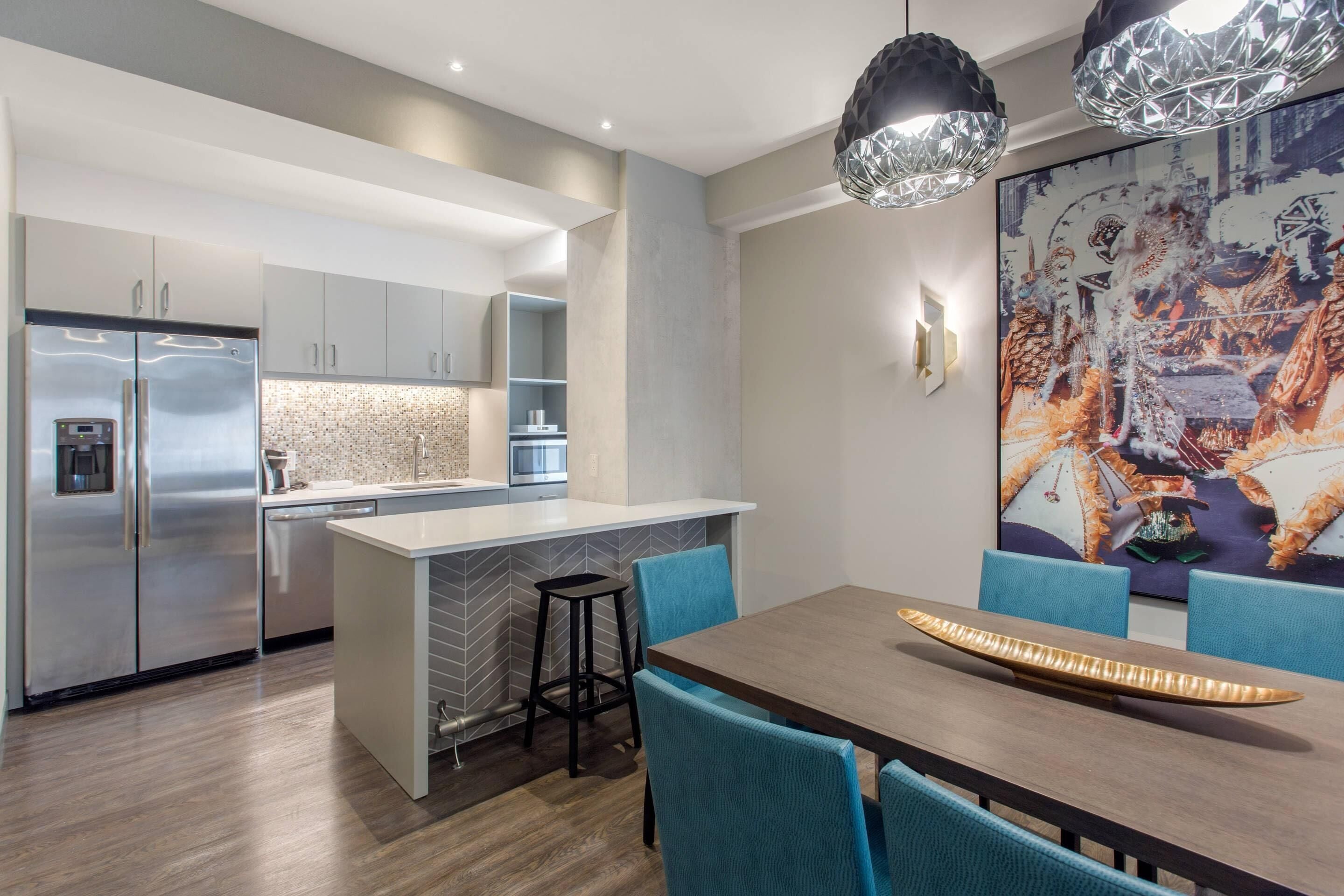 A modern kitchen with a central island, stainless steel appliances, and a dining area with blue chairs and a wooden table.