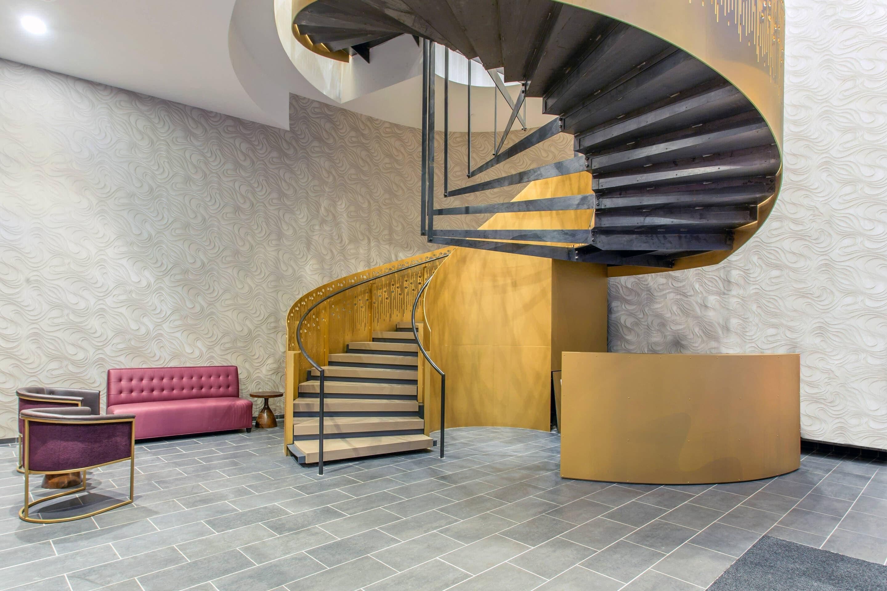 A modern interior with a spiral staircase, a pink sofa, and a round reception desk.