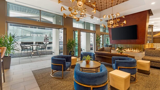 A spacious lobby with a modern chandelier, comfortable seating, a flat-screen TV, and a large window overlooking the street.