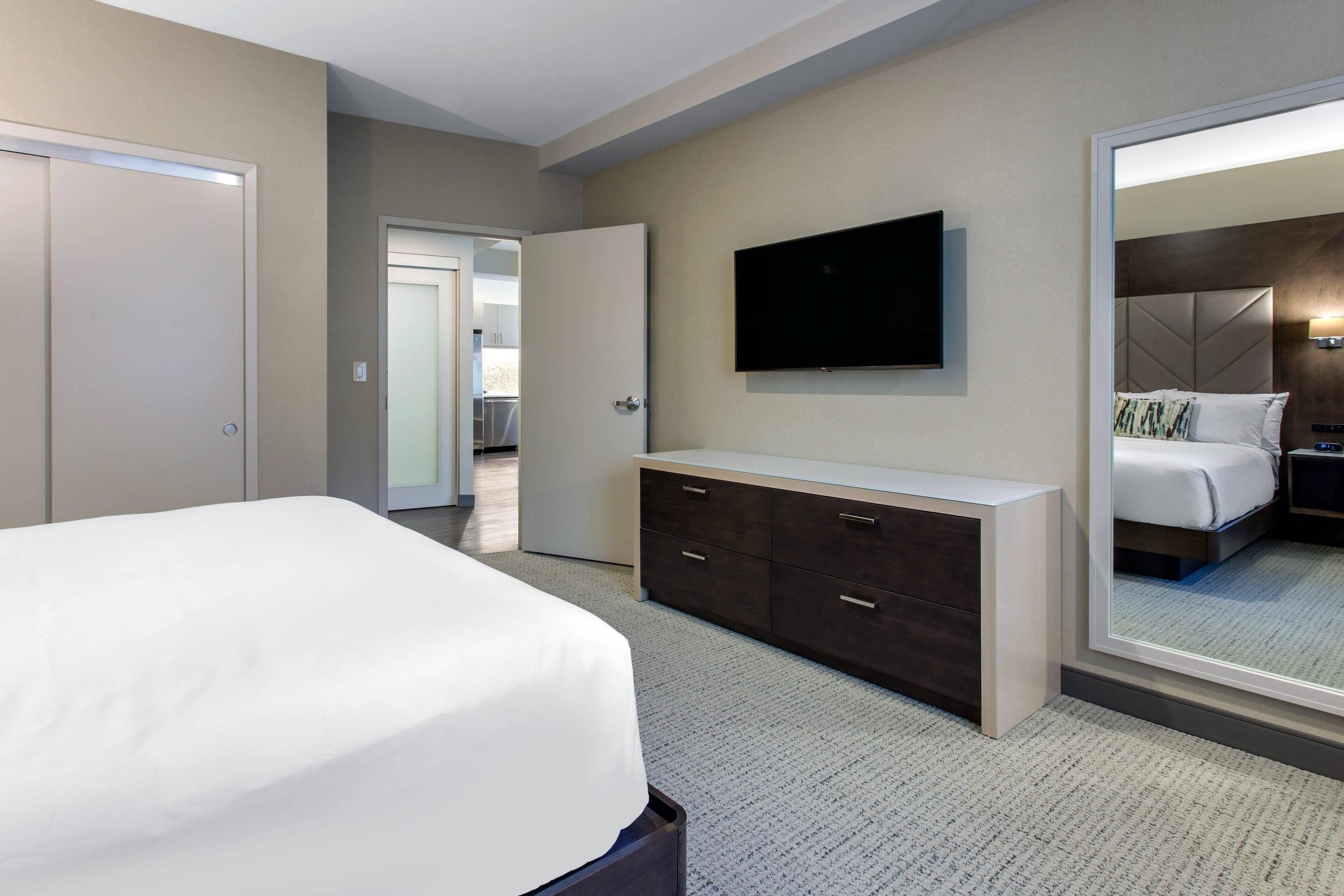 A modern hotel room with a large bed, a dresser, a television, and a mirror.