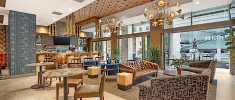 A modern hotel lobby with a bar area, seating arrangements, and large windows offering views of the city.