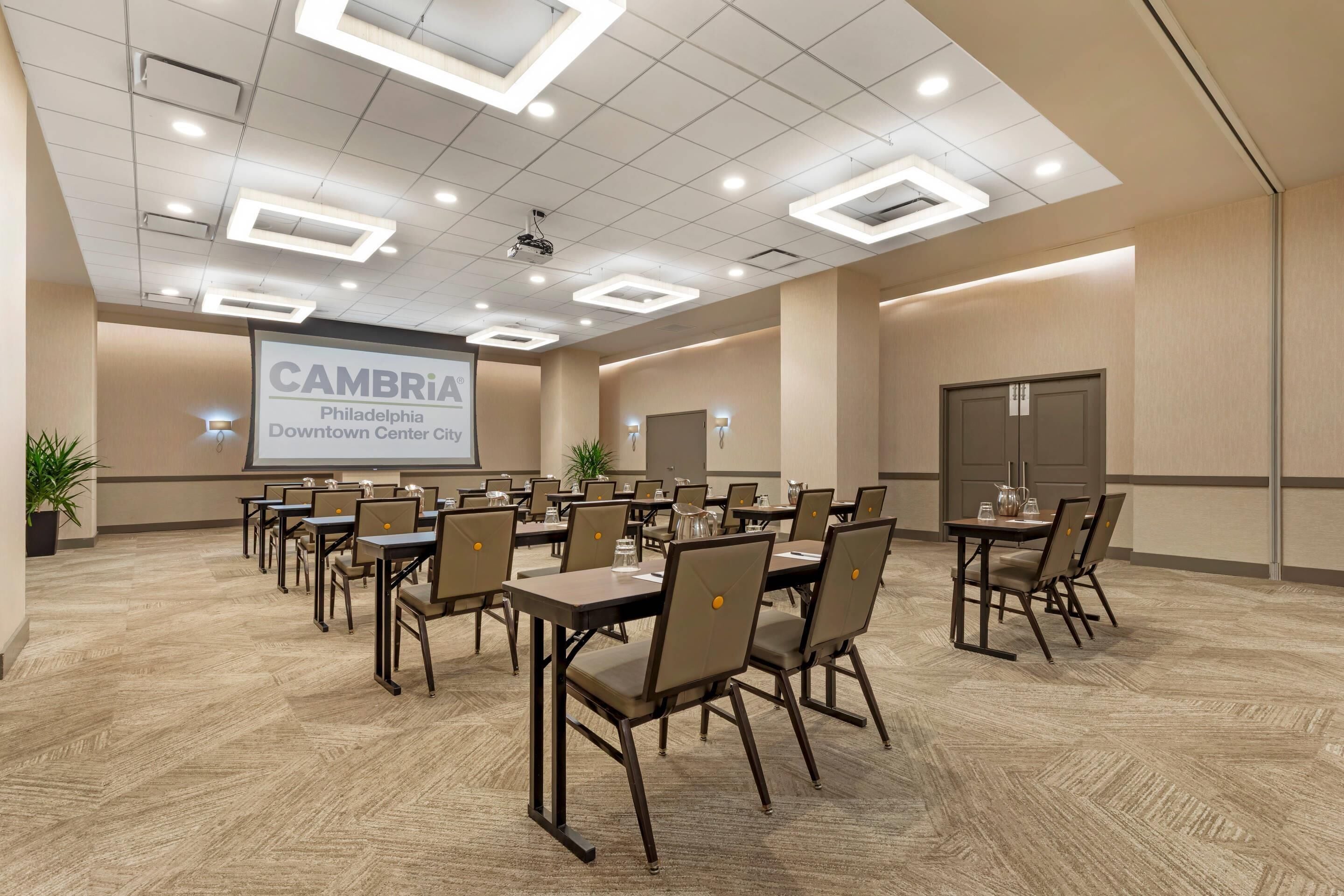 A conference room with multiple tables and chairs, a projector screen, and a presentation on the wall.