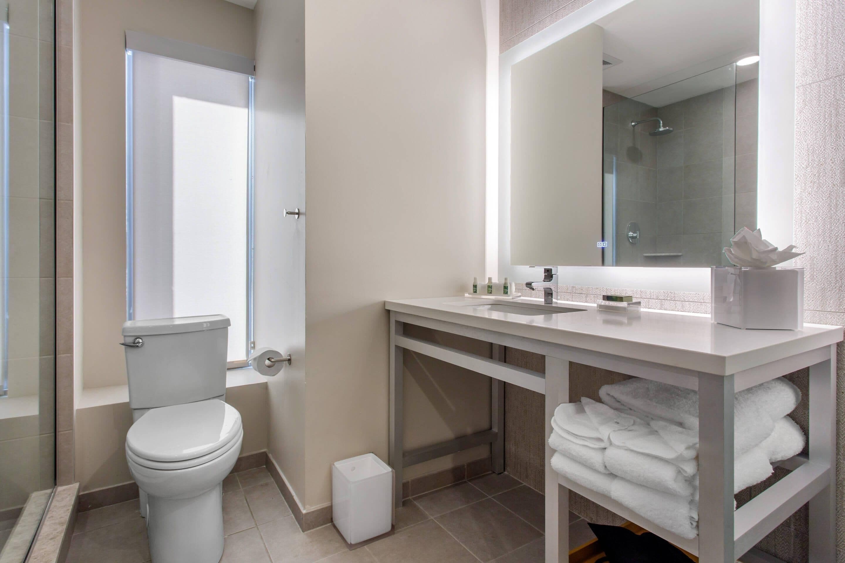 Ein modernes Badezimmer mit Toilette, Waschbecken, Spiegel und Ablage für Handtücher.