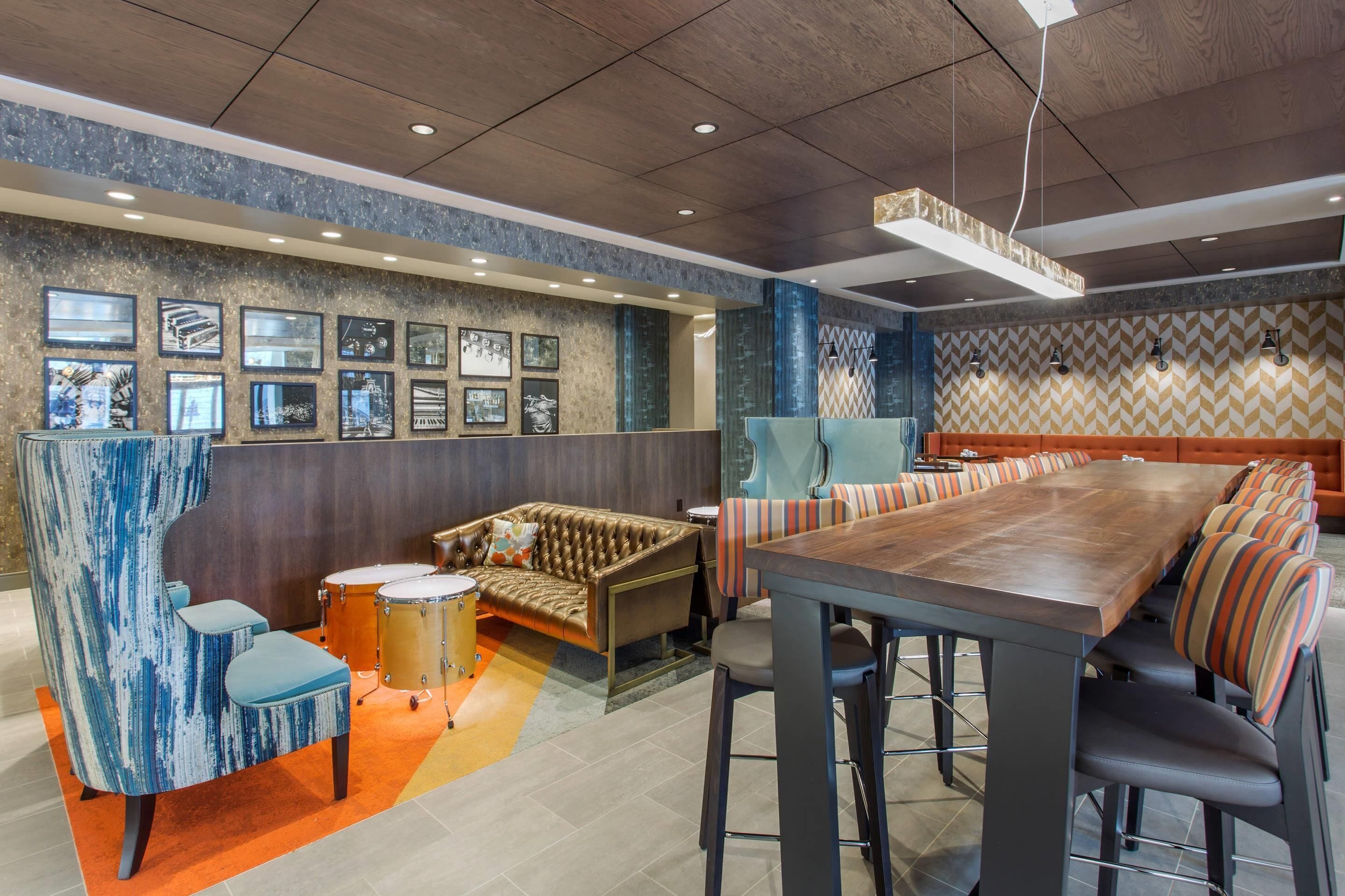 Una sala de reuniones moderna con una larga mesa, asientos acolchados, un set de batería y cuadros en las paredes.