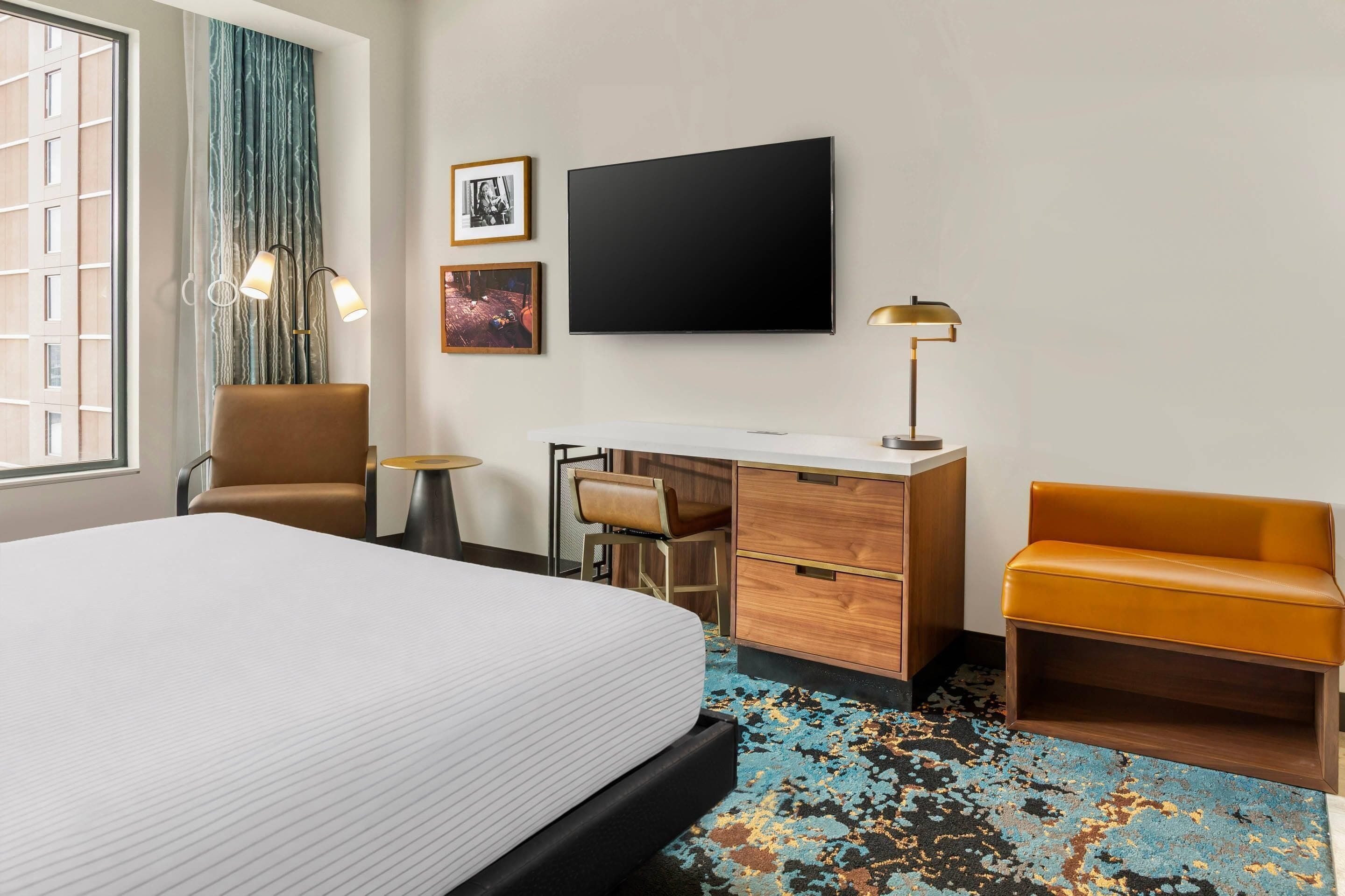 Habitación de hotel con una cama grande, un escritorio con silla, un sofá, un televisor de pantalla plana y una ventana con cortinas.