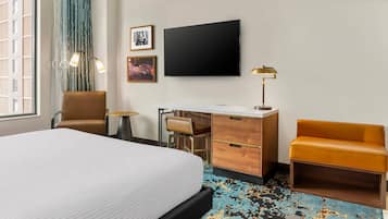 Habitación de hotel con una cama grande, un escritorio con silla, un sofá, un televisor de pantalla plana y una ventana con cortinas.