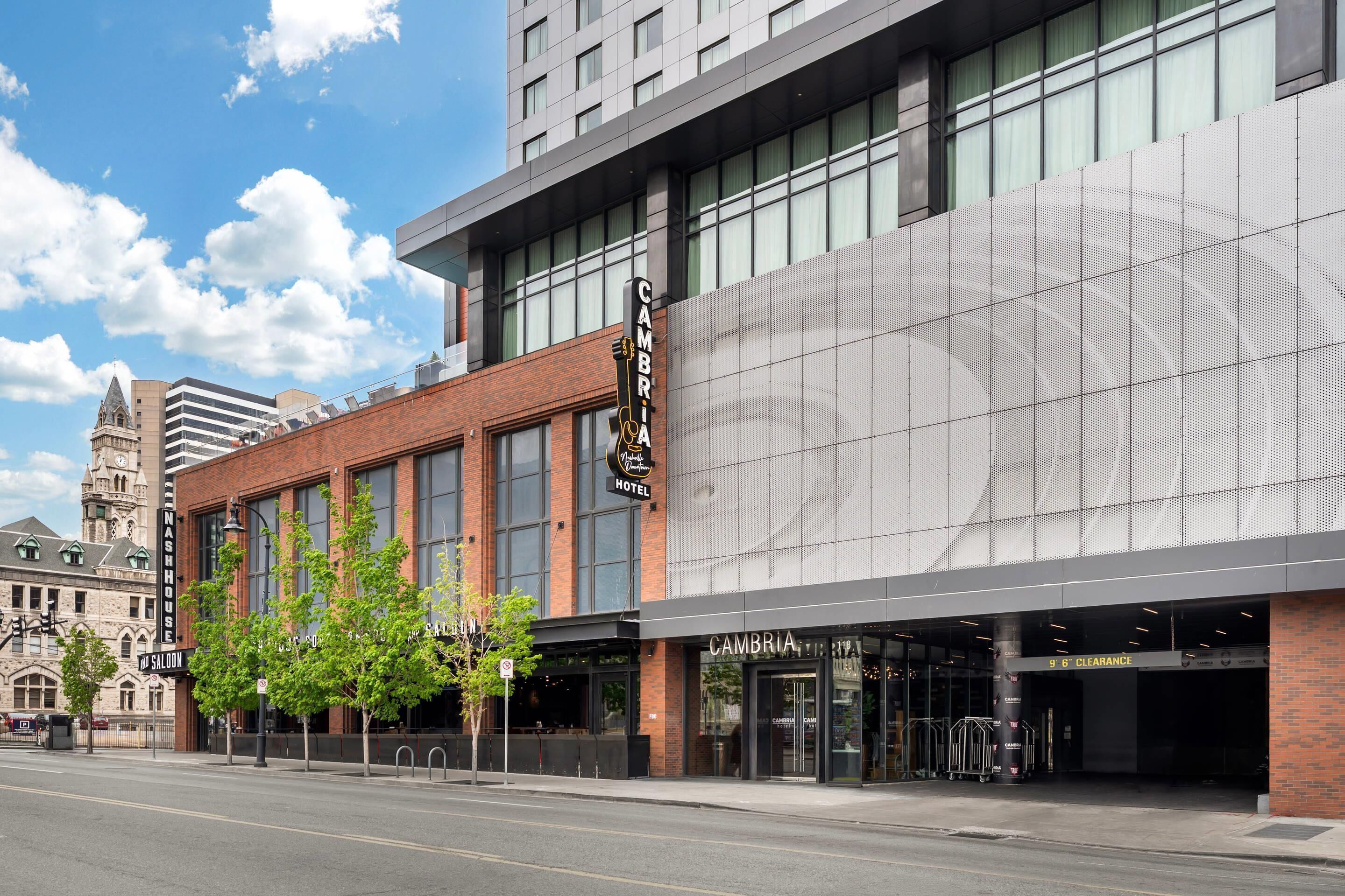A modern hotel with a large sign, a clear entrance, and a historic building in the background.