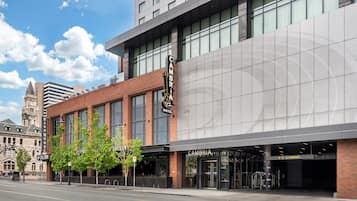 A modern hotel with a large sign, a clear entrance, and a historic building in the background.