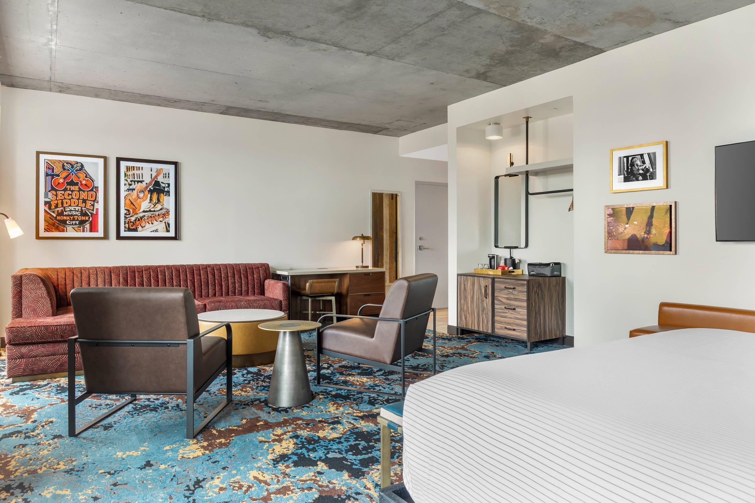 Habitación de hotel con cama, sofá, sillón, escritorio, cómoda y dos carteles enmarcados en la pared.