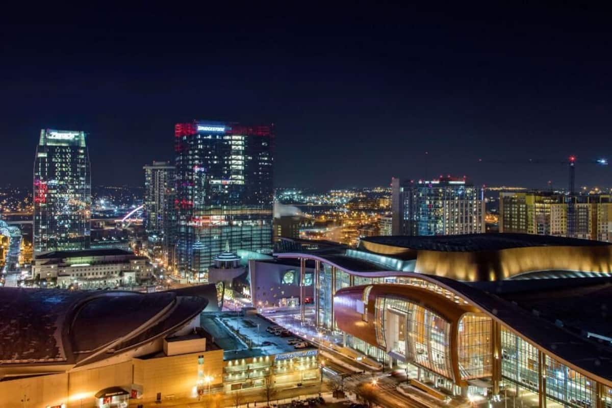 A cityscape at night with illuminated skyscrapers and a modern building with a curved roof.