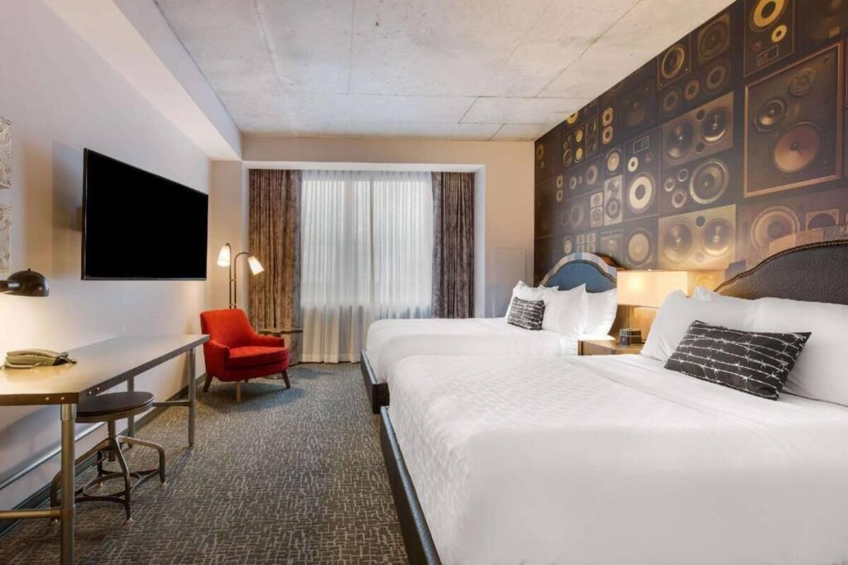 A hotel room with a bed, a desk, a chair, a TV, and a wall with circular patterns.