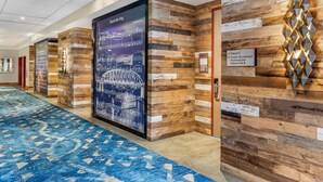 Corridoio di un hotel con tappeto a motivi blu, pannelli murali in legno e un grande poster del Nashville Riverwalk.