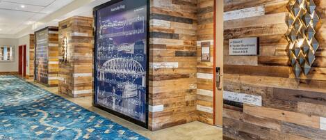 Un pasillo de hotel con alfombra de diseño azul, paneles de madera y un cartel grande del Nashville Riverwalk.