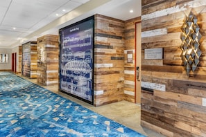 A hotel corridor with a blue patterned carpet, wooden wall panels, and a large poster of the Nashville Riverwalk. - Cambria Hotel Nashville Downtown (Nashville)