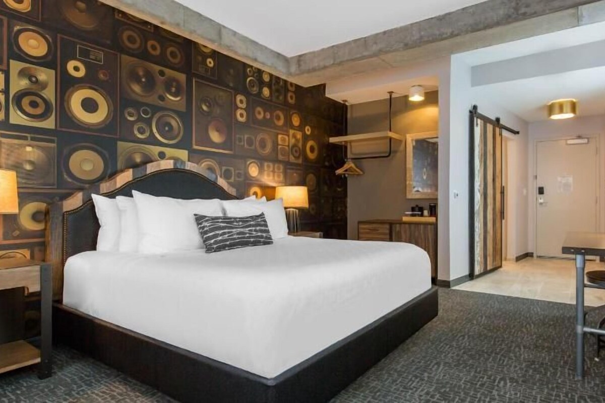 A hotel room with a large bed, a desk, a TV, and a wall with circular patterns.