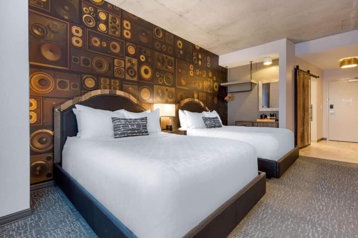A hotel room with two beds, a patterned wall, a mirror, and a door.