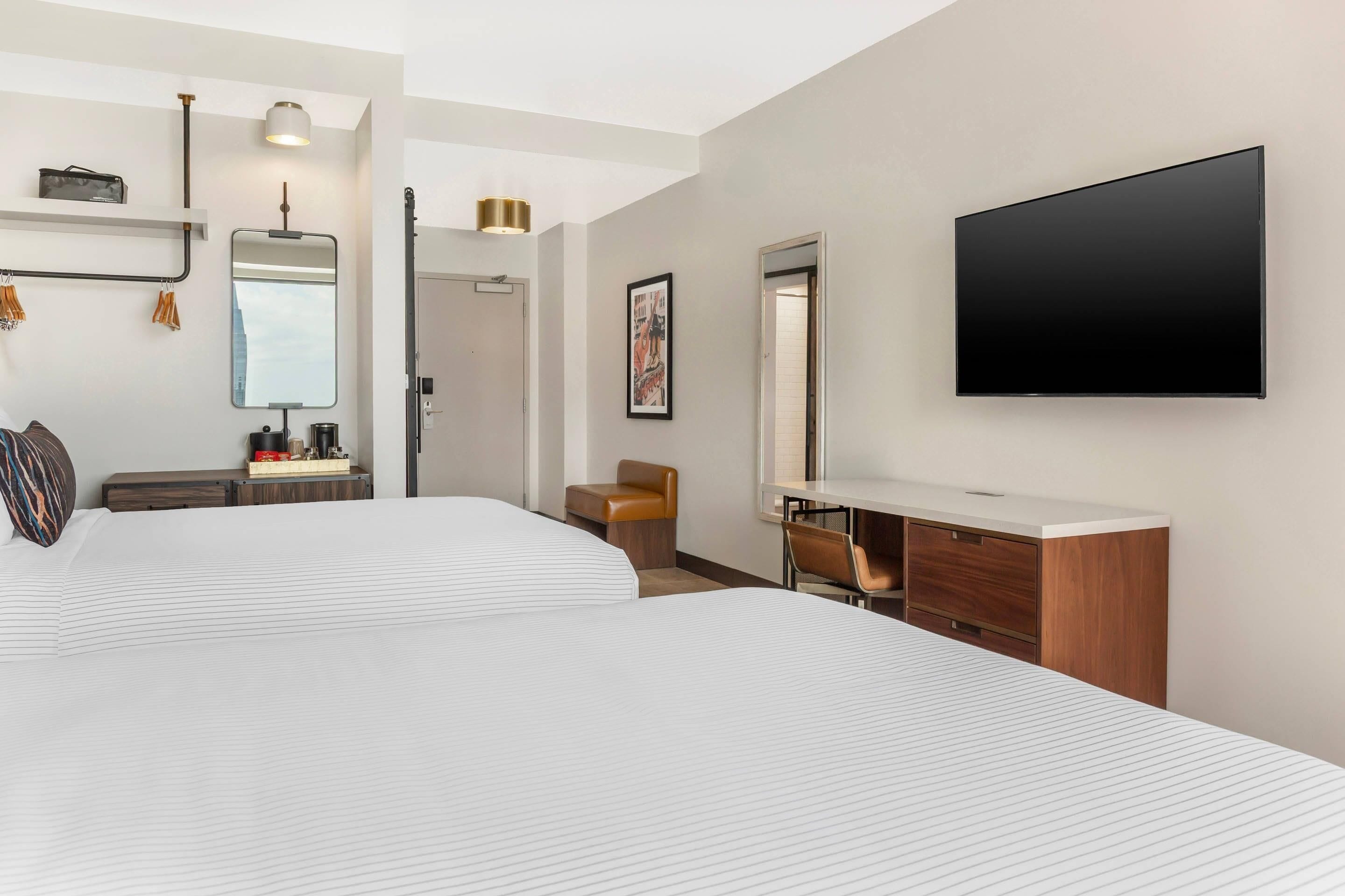 Una habitación de hotel moderna con una cama grande, un escritorio, una silla, un televisor de pantalla plana y un espejo.