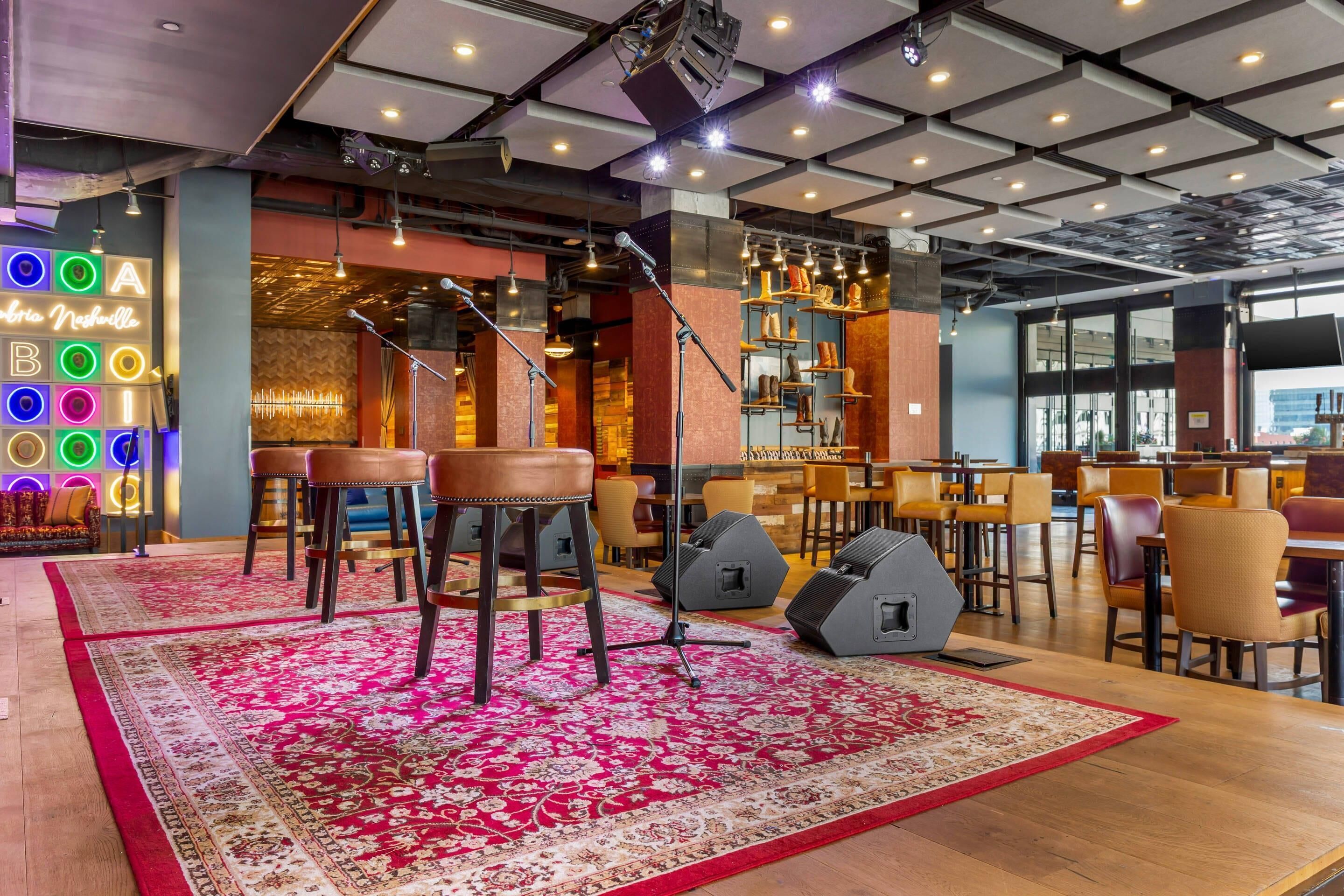A modern bar area with stools, a large rug, and a neon sign.
