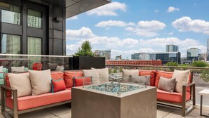 Una terrazza sul tetto con ringhiera in vetro, un divano rosso, un tavolo quadrato e vista sulla città.