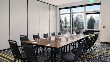 A conference room with a large table, chairs, and a view of trees through the windows.