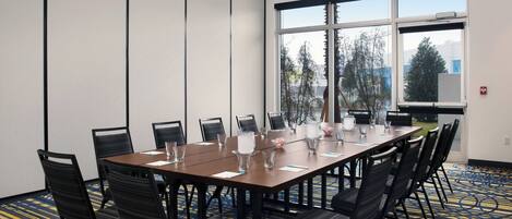 A conference room with a large table, chairs, and a view of trees through the windows.
