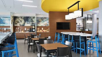 Ein modernes Restaurant mit blauen Barhocker, Holztischen und einer gelben Akzentwand.