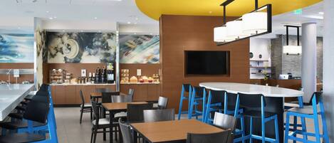 A modern restaurant with blue bar stools, wooden tables, and a yellow accent wall.