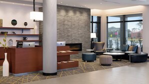 A modern reception area with a wooden desk, a fireplace, comfortable seating, and large windows offering a view. - Fairfield Inn & Suites by Marriott Daytona Beach Speedway/Airport (Daytona Beach)