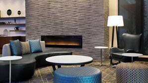 A modern lounge area with a stone wall, a fireplace, leather sofas, round tables, and a patterned ottoman. - Fairfield Inn & Suites by Marriott Daytona Beach Speedway/Airport (Daytona Beach)