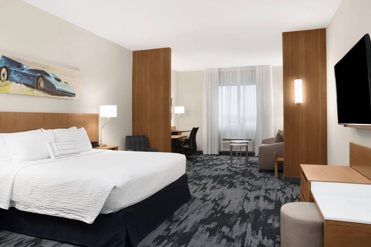 A hotel room with a large bed, a desk, a chair, a TV, and a painting on the wall.