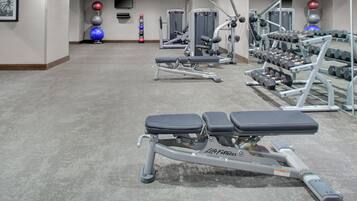 Un gimnasio con equipamiento de ejercicio, bancos y un espejo grande.