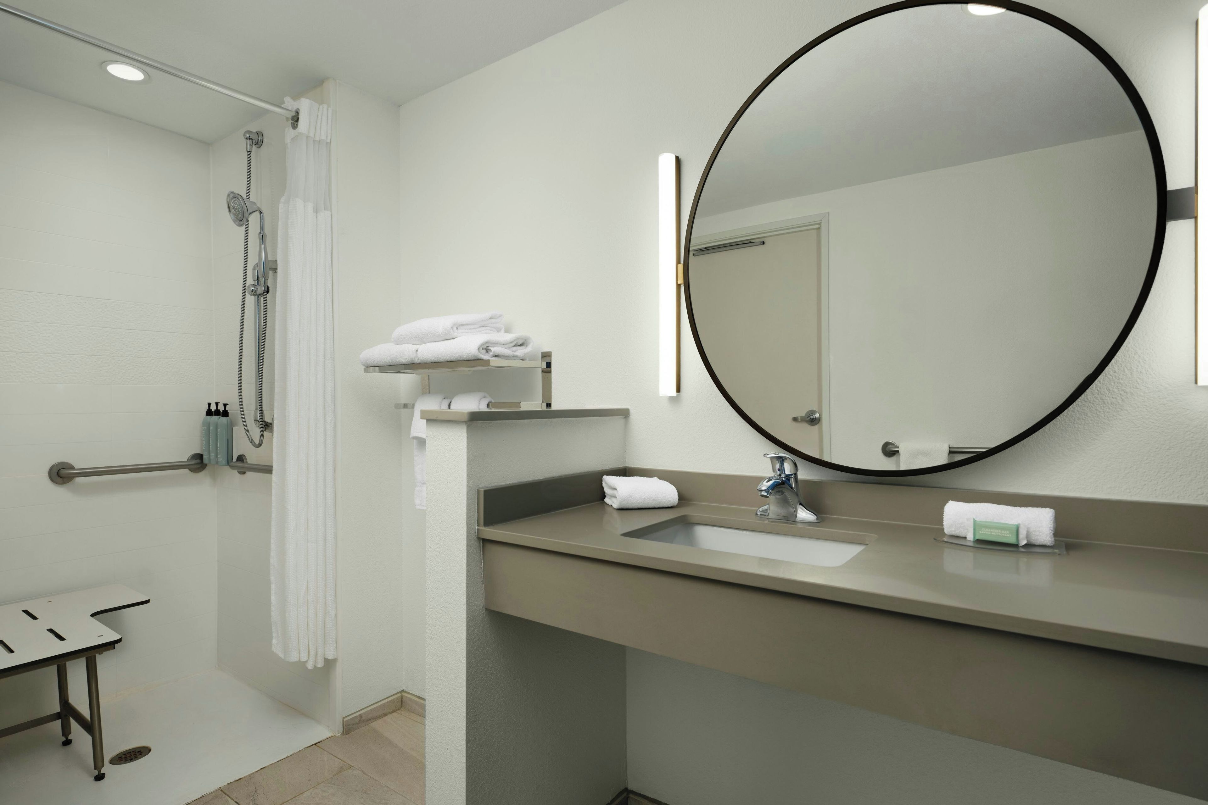 Un baño con ducha, lavamanos, espejo y perchero.