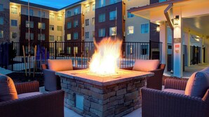 A stone fire pit surrounded by wicker chairs in an outdoor patio area of a multi-story building. - Fairfield by Marriott Inn & Suites Boulder Broomfield/Interlocken (Broomfield)