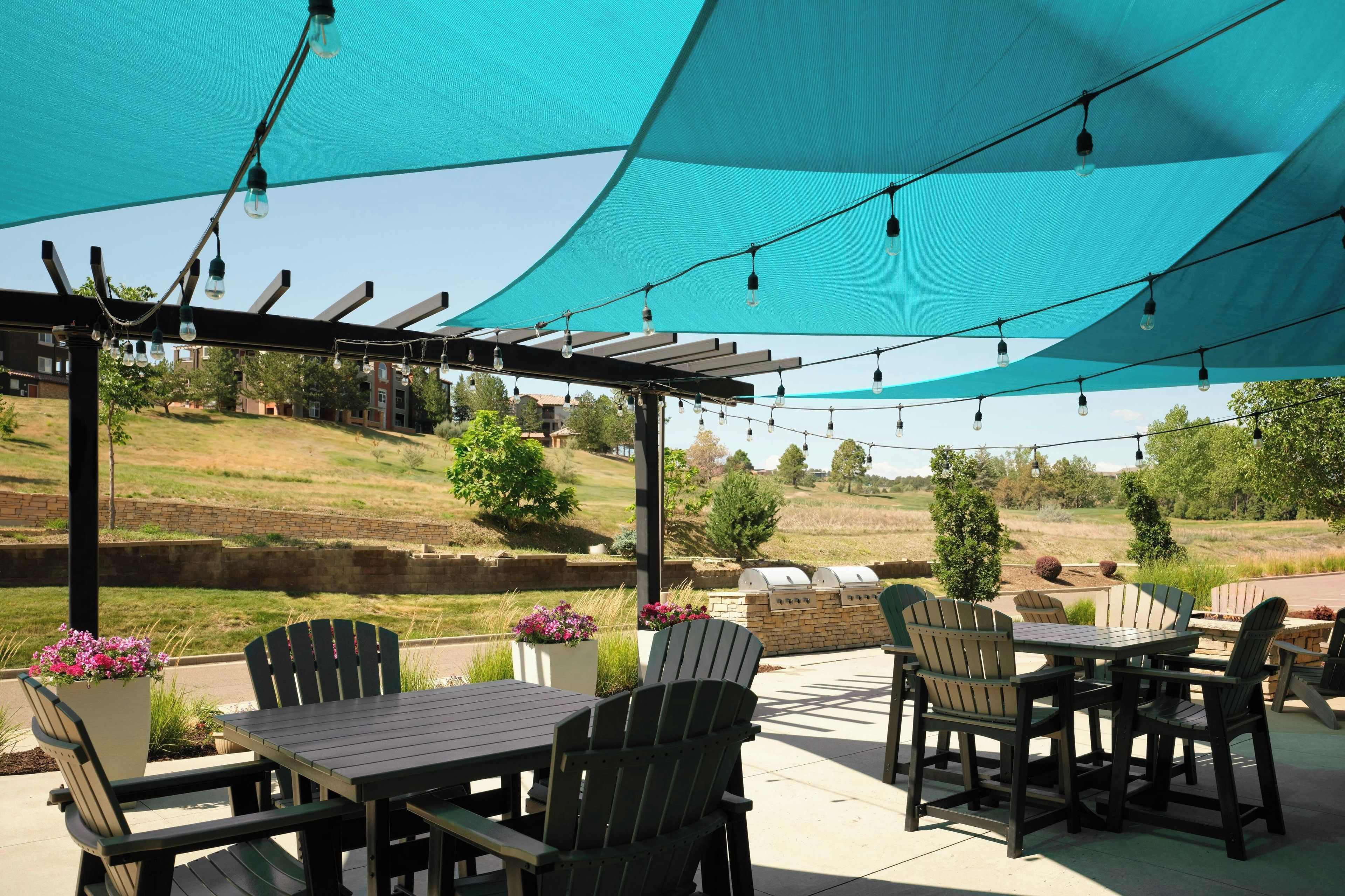 An outdoor patio with tables and chairs, a pergola, and string lights.