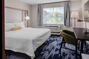Habitación de hotel con cama, escritorio, silla, ventana con cortinas y equipo de aire acondicionado.