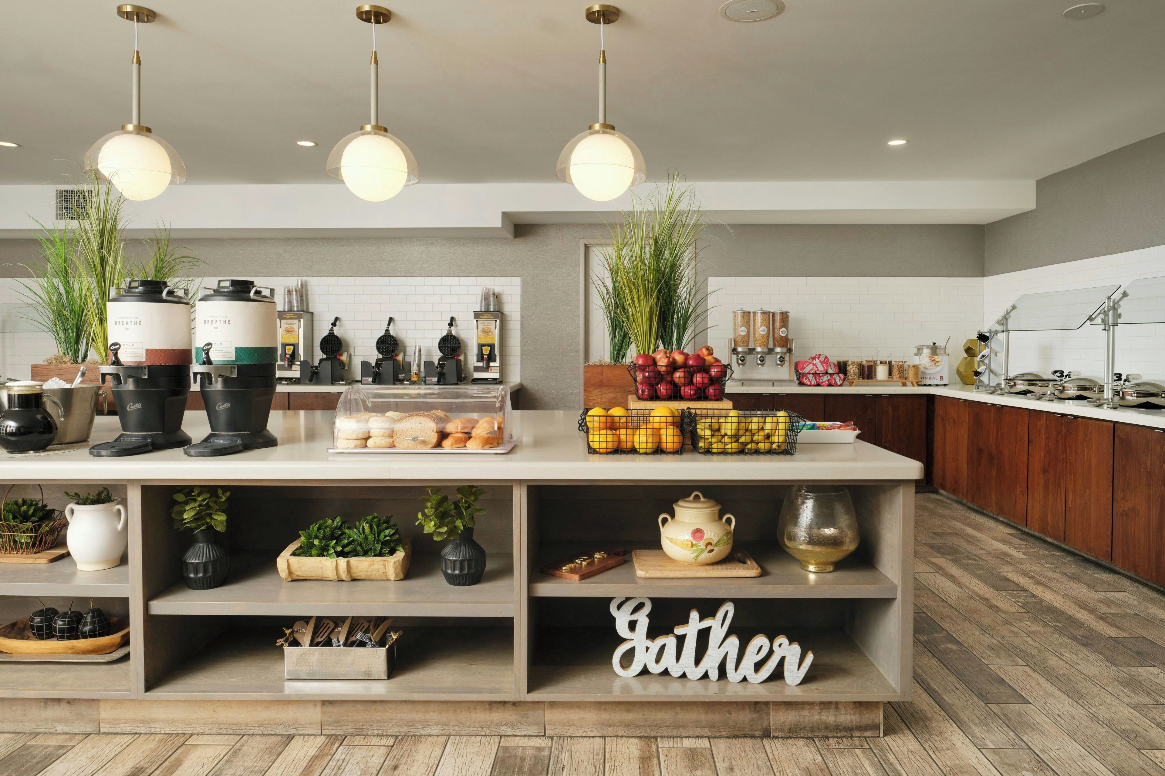 A modern kitchen with a central island, various appliances, and a 'Gather' sign on the lower shelf.