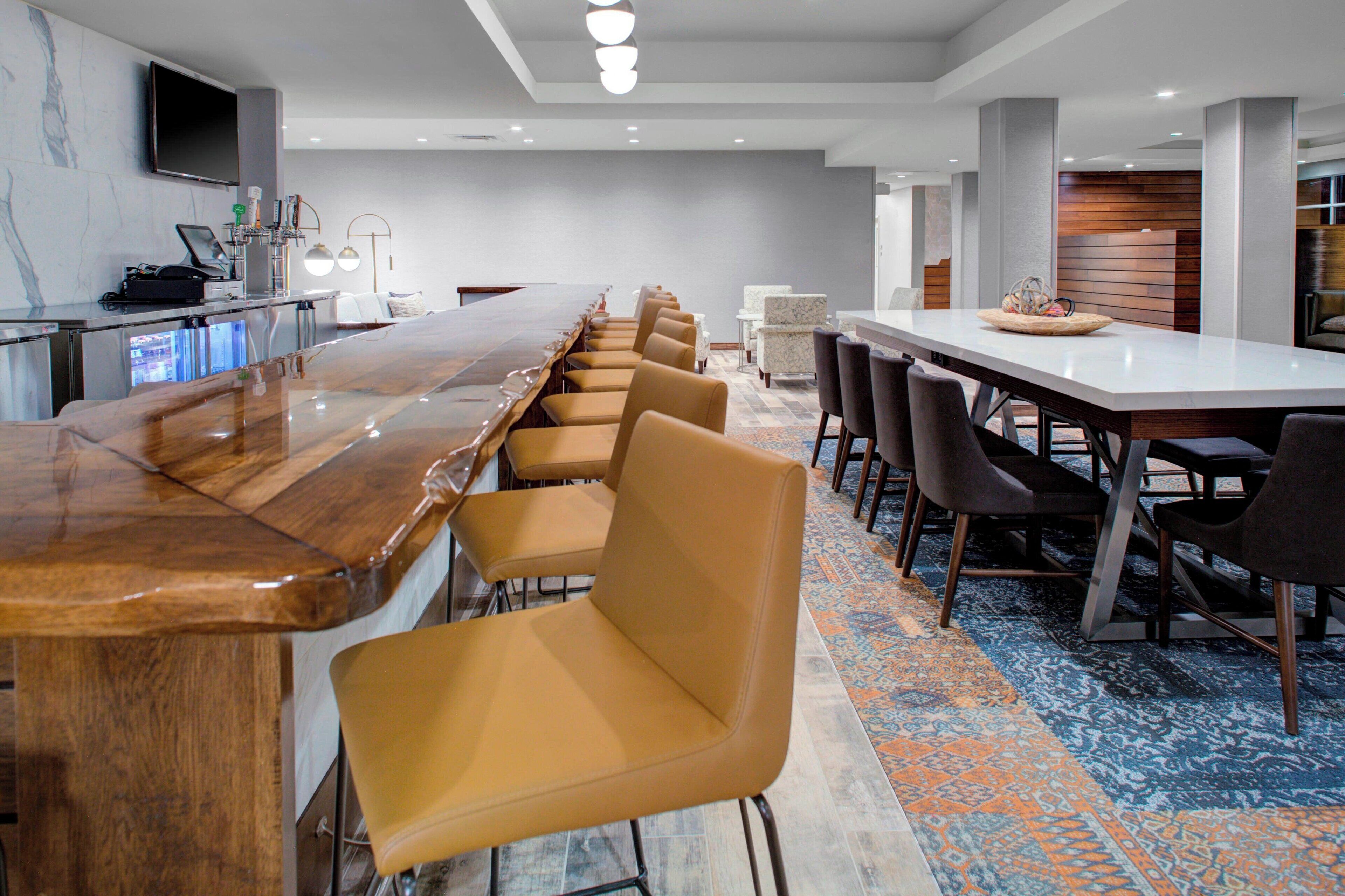 Un salón de conferencias moderno de hotel con una larga mesa de madera, varias sillas, una televisión y una zona de bar.