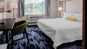 A hotel room with a bed, a desk, a chair, a lamp, a window with curtains, and an air conditioning unit. - Fairfield by Marriott Inn & Suites Boulder Broomfield/Interlocken (Broomfield)