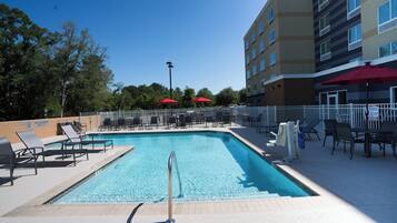 A swimming pool with lounge chairs and umbrellas, surrounded by a fence and trees.