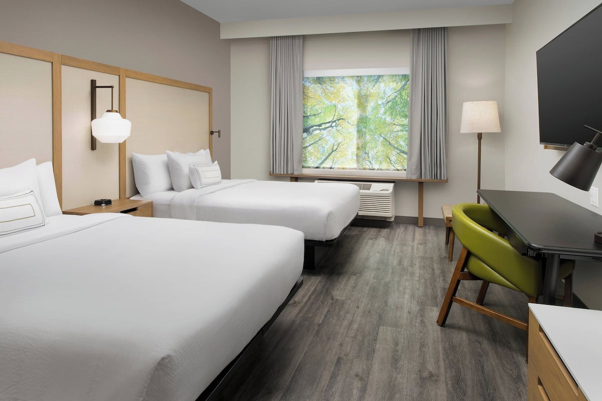 A hotel room with two beds, a desk, a chair, a TV, and a window with curtains.