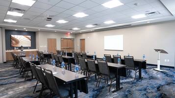 A conference room with tables, chairs, water bottles, a projector screen, and a carpeted floor.