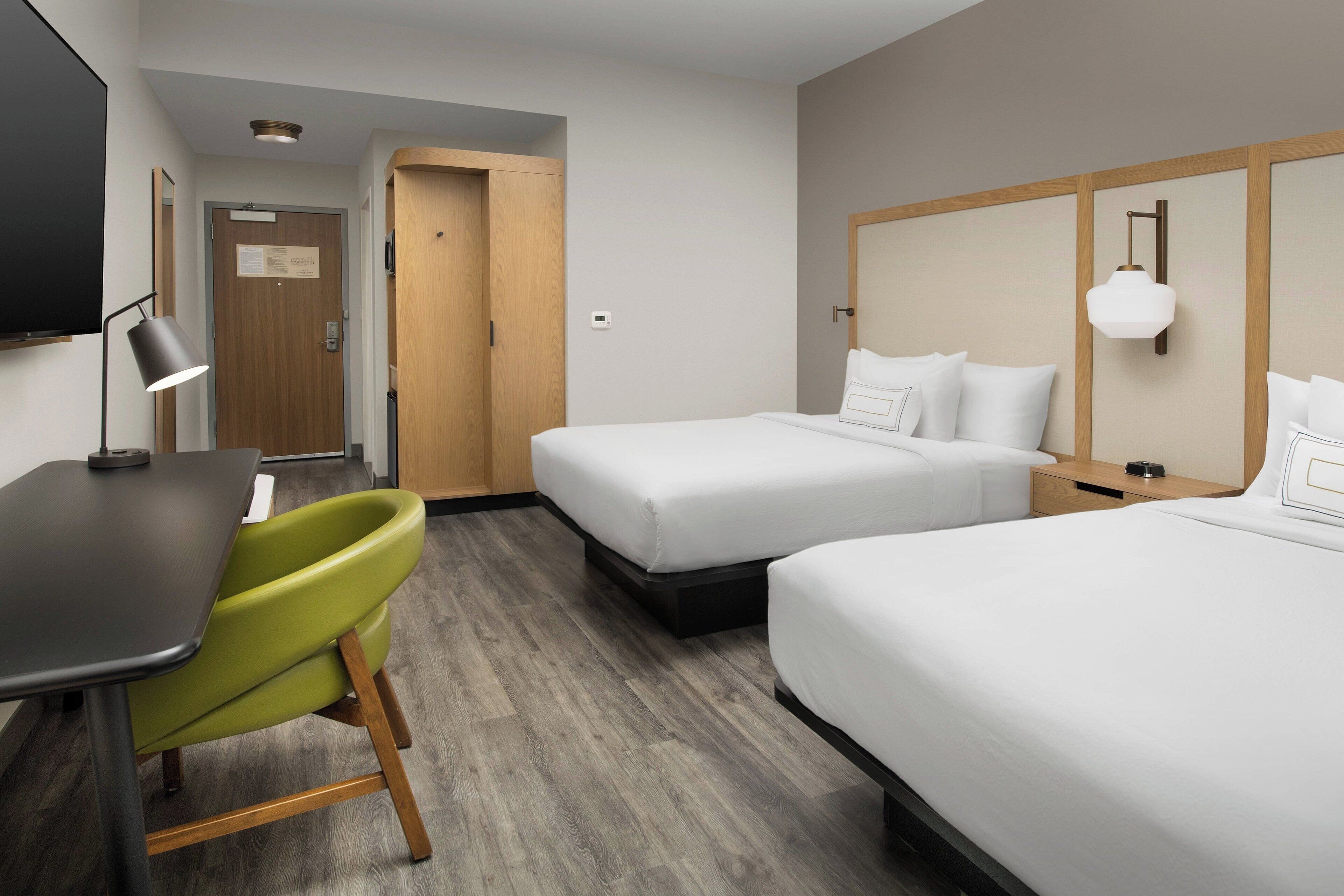 A hotel room with two beds, a desk, a chair, and a television.
