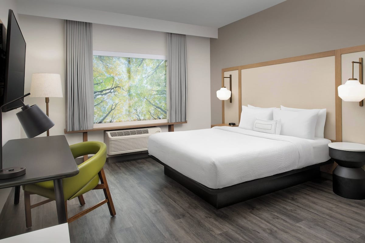 A hotel room with a bed, a desk, a chair, a TV, and a window with curtains.
